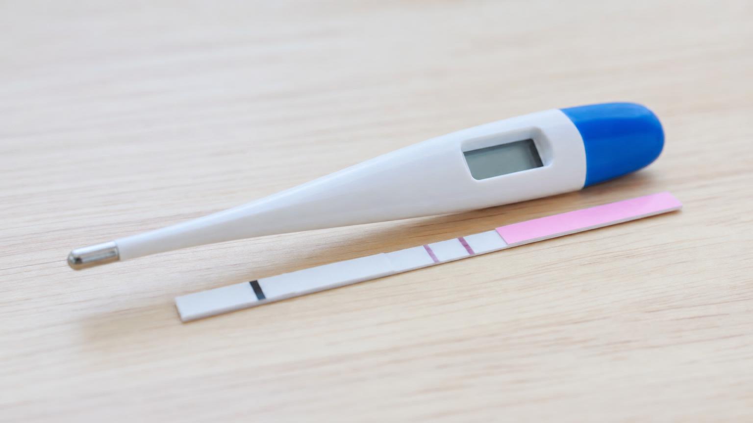 木の台に並べて置かれた排卵検査薬と基礎体温計